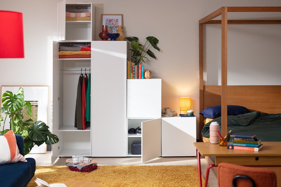 White modular wardrobe in bedroom with compartments for folded and hanging garments.